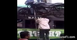 هندي يرفع دراجة نارية على رأسه إلى أعلى حافلة (فيديو)